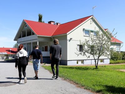 Taustalla Kankaanpään A-kodin miljöön rakennus. Etualalla kolme henkilöä kävelemässä kohti rakennusta.