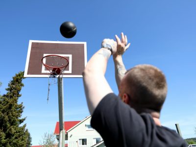 Kankaanpään A-kodin pihalla henkilö heittämässä koripalloa koriin.