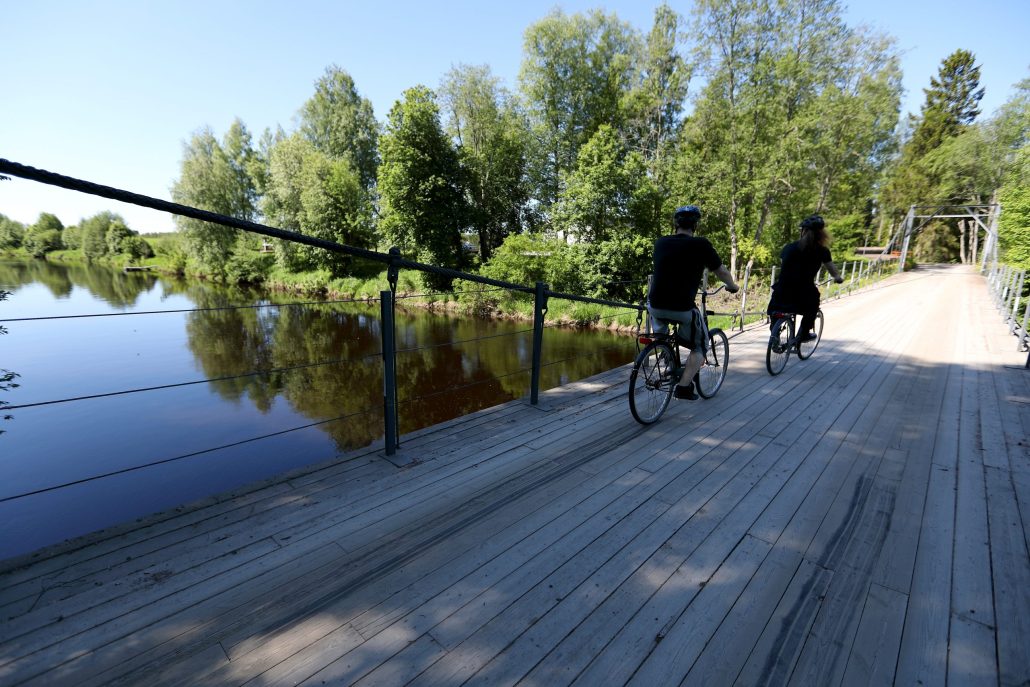 Henkilöt pyöräilemässä puista siltaa pitkin veden yli .
